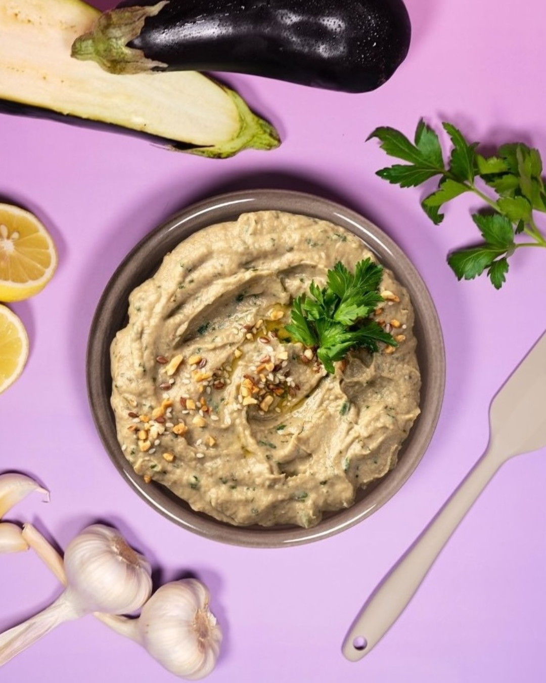 Baba Ganoush Auberginencreme angerichtet in einer Schale und dekoriert mit Auberginen Knoblauch und Zitronen
