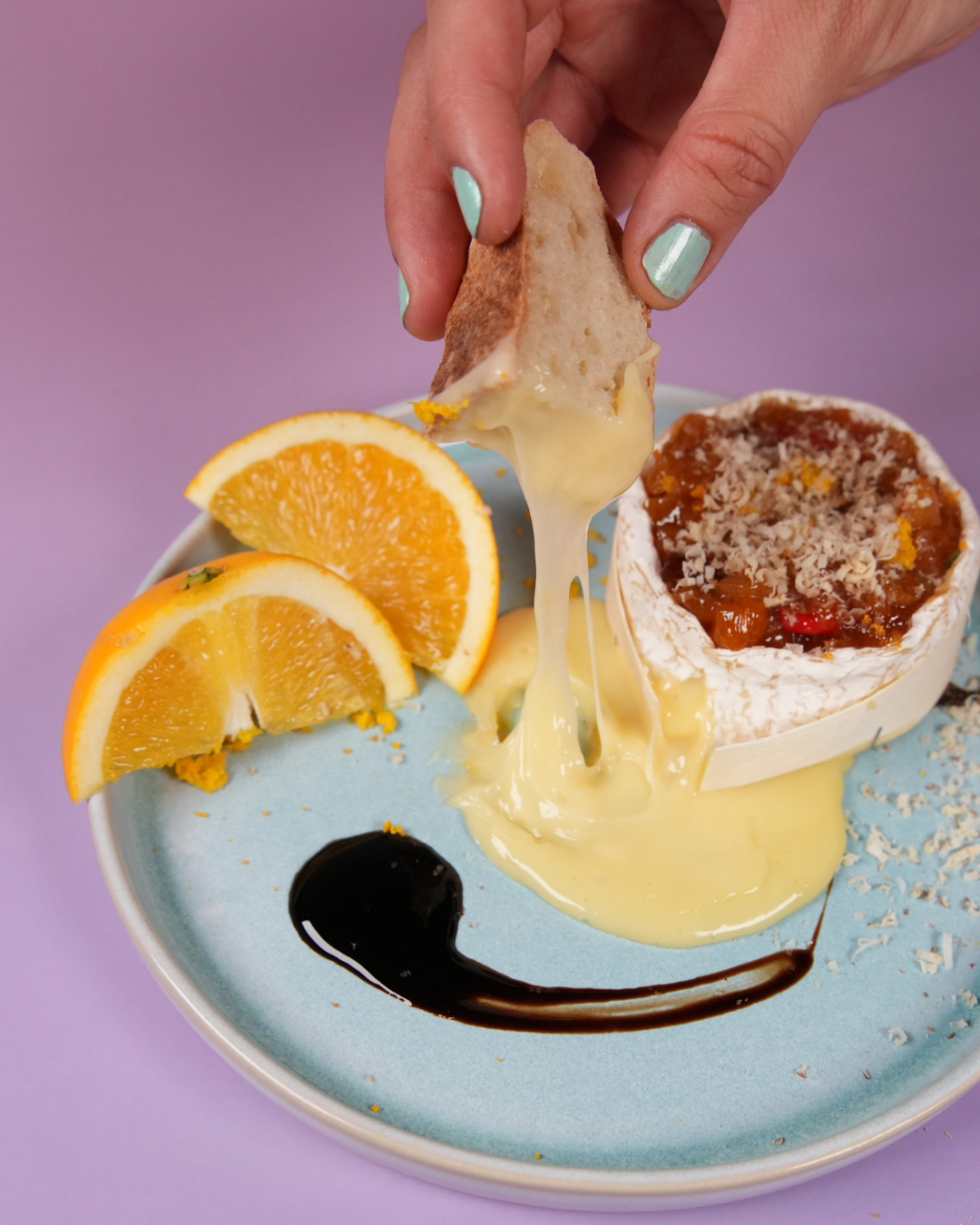 Gebackener Camembert im Ofen mal anders mit Aprikosencreme & Nussflocken auf einem Teller serviert und mit Orangenscheiben dekoriert