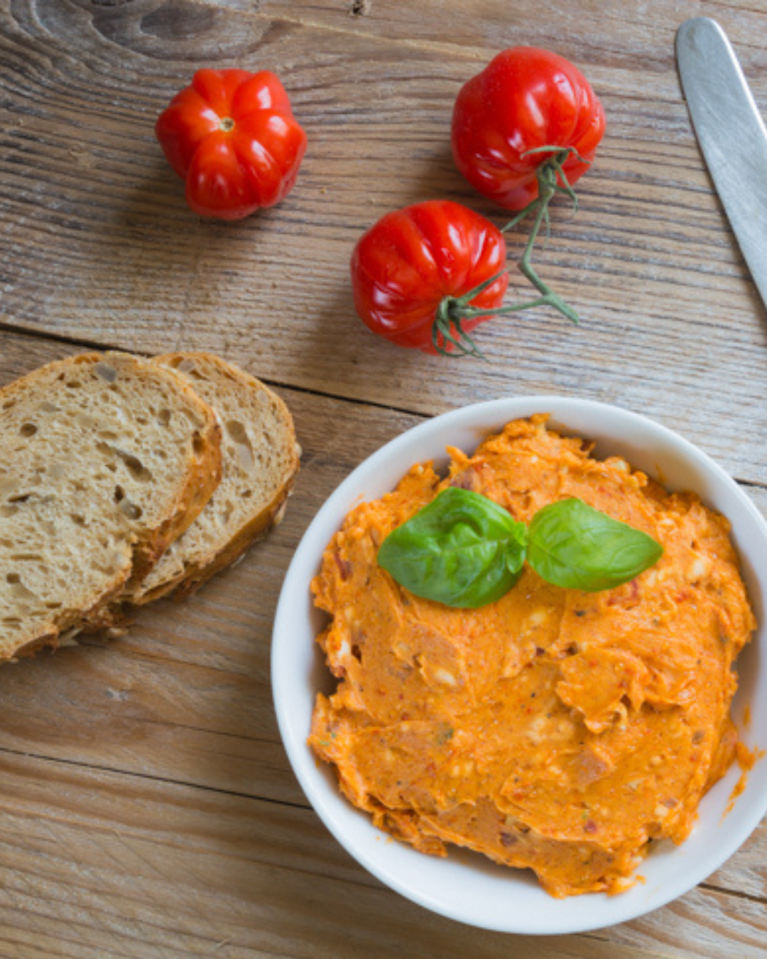 Tomatenbutter cremig in einer Schüssel angerichtet mit Broten und frischen Tomaten dekoriert